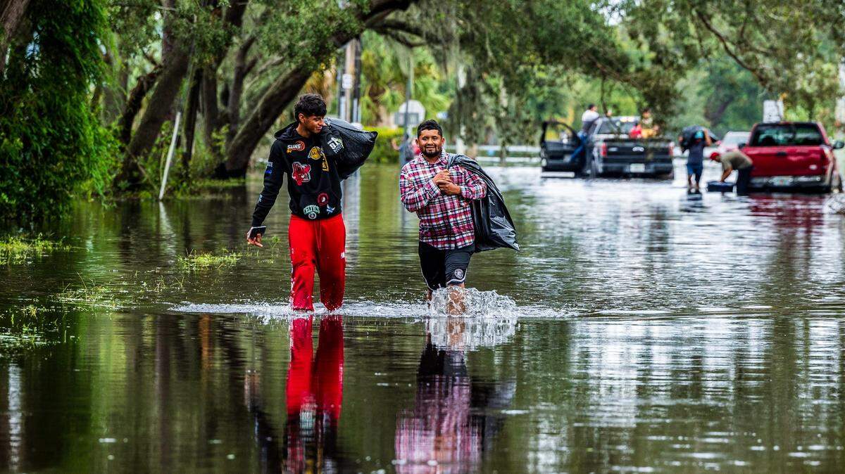 Juan José Muñoz (izq.) y Elvin Antonio Urbina caminan con sus pertenencias por la inundada N 15 St in North Tampa, el 10 de octubre de 2024.