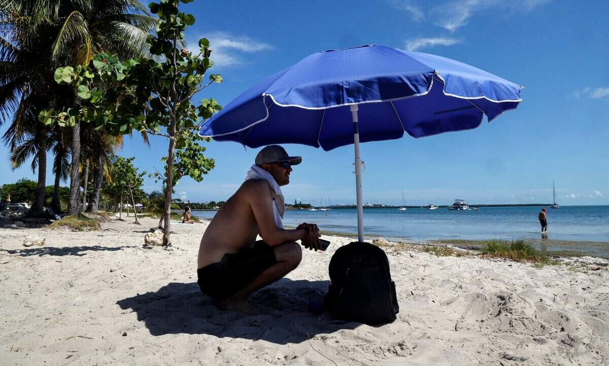 Michelangelo Manganelli sits under the shade of his umbrella to avoid the hot sun on the beaches along Rickenbacker Causeway in Miami, Florida on Thursday, June 6, 2024.