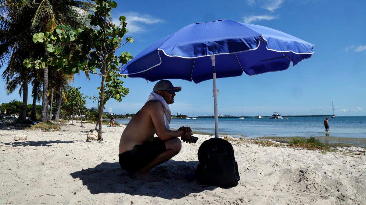 MICHELANGELO MANGANELLI, un turista, se sienta bajo la sombra de su paraguas para evitar el sol abrasador en las playas de Rickenbacker Causeway en Miami el 6 de junio de 2024.