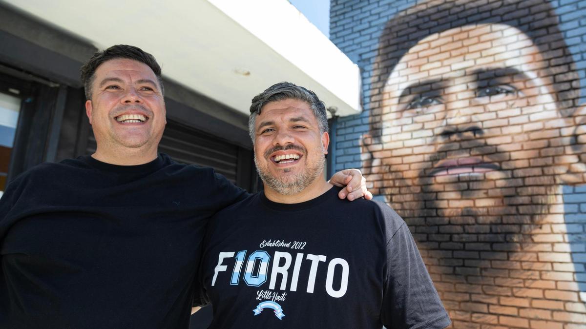 Los hermanos Cristian Álvarez (izquierda) y  Maximiliano Álvarez son los propietarios del restaurante y bar Fiorito en el Pequeño Haití., afuera de su restaurante en Miami junto a un mural de Lionel Messi el 12 de julio de 2023.