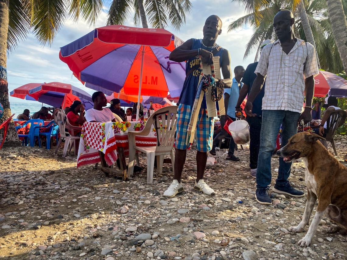 Vendors show off their wares as people enjoy food and drink on the beach in Jacmel.
