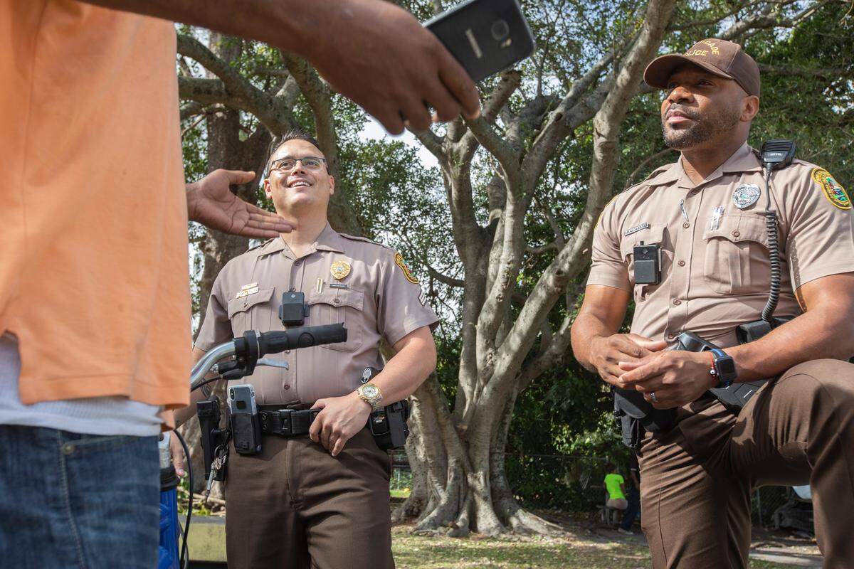 Miami-Dade Sergeant Jason Waite, left, and officer Zuri Chambers talk with resident Nick Freeman during a stop in Broadway Park on Friday, Dec. 28, 2018, during a patrol for Operation Blue and Brown, a joint effort with Miami that has seen significant staffing cuts in recent months.