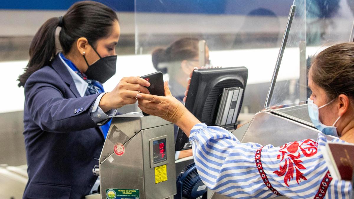 A traveler shows an American Airlines employee her phone to prove she is vaccinated, using VeriFLY, a smartphone app that lets people upload documentation proof of negative COVID test or vaccine proof, while checking in before her international flight at Miami International Airport in Miami, Florida, on Monday, June 7, 2021.