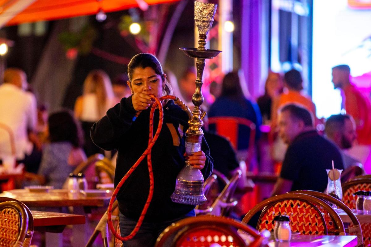An employee moves a hookah pipe at the outdoor patio of Ocean’s Ten on Ocean Drive in Miami Beach on Dec. 1, 2022. Because the patio area is on private property and not on the public sidewalk, the bar can work around a city ban on hookah at sidewalk cafes.