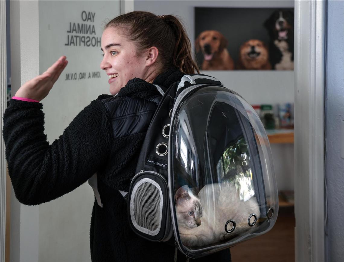 Erika Garcia waves goodbye as she carries Tofu the cat inside her Cat Bag at Yao Animal Hospital in Miami.