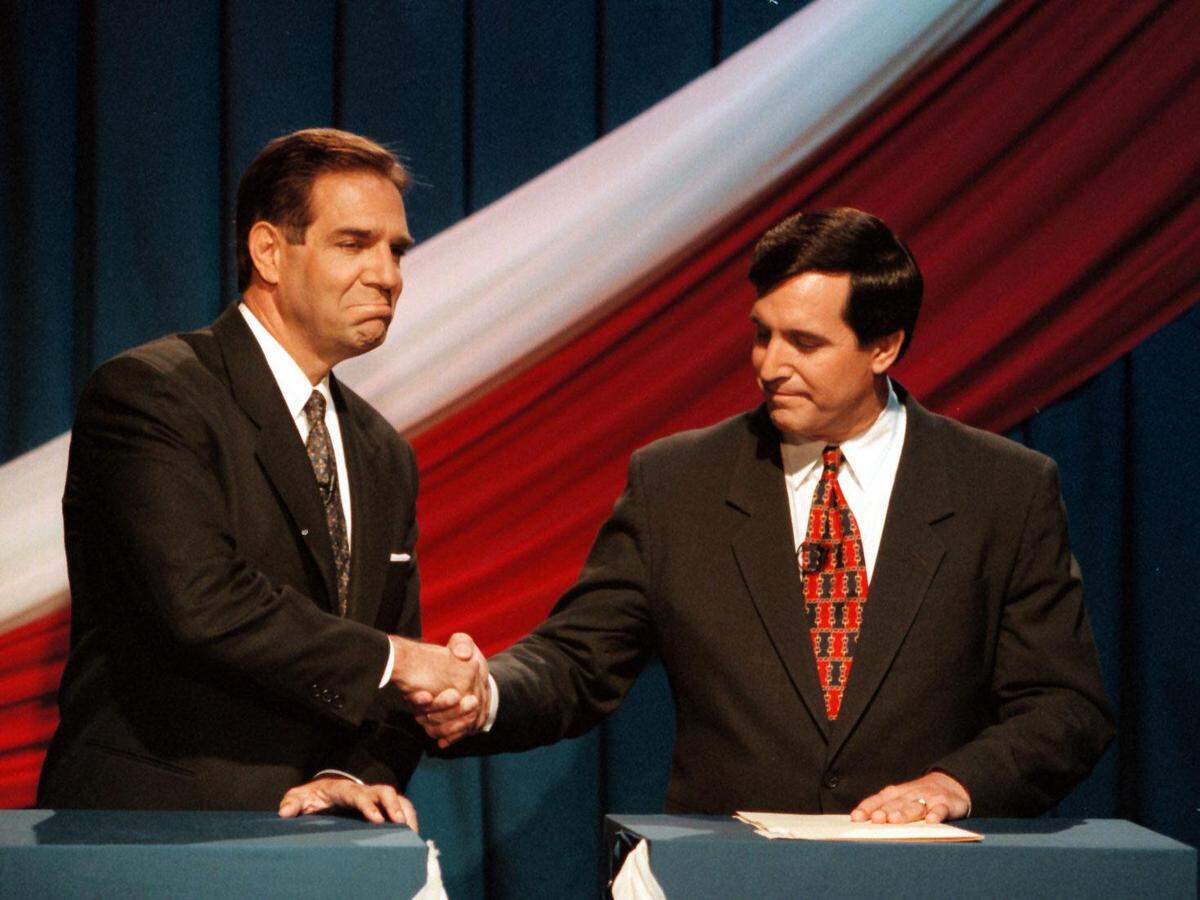 In a photo from Oct. 24, 1997, the two main candidates for Miami mayor, Xavier Suarez, left, and Joe Carollo, right, shake hands while avoiding each other’s eyes.