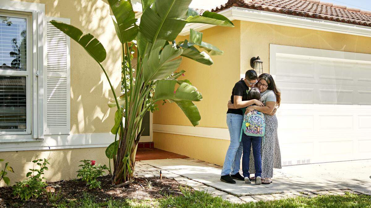 A family hugging their young daughter outside their home before she goes to school. 