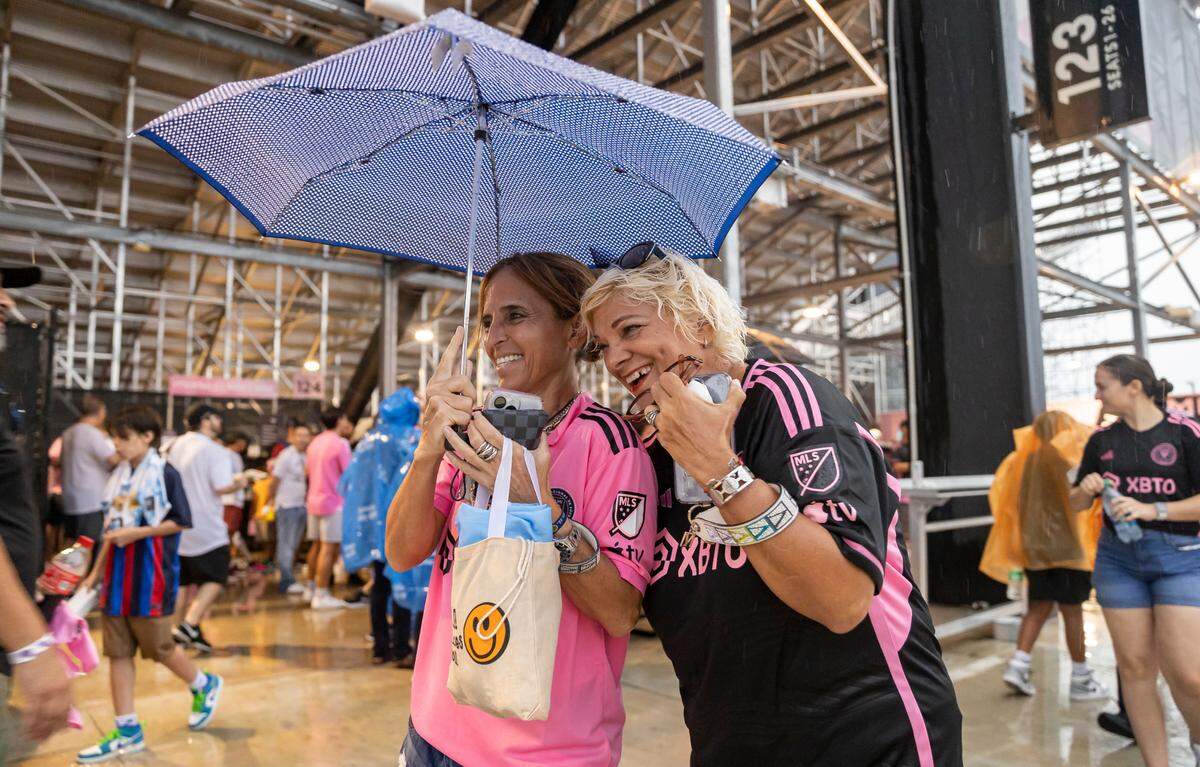 Andrea Monzani, left, and Emma Morales try to stay dry during a weather delay before the start of Inter Miami’s The Unveil at DRV PNK Stadium on Sunday, July 16, 2023, in Fort Lauderdale, Fla. The event was held to officially welcome Argentine forward Lionel Messi and Spanish midfielder Sergio Busquets to the team.