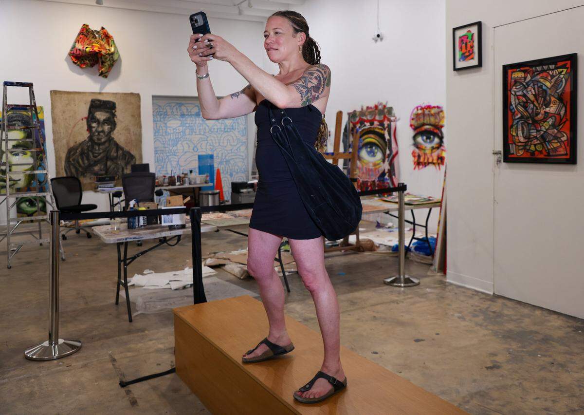 Artist Laura Page, who is visiting from Brooklyn, NY, left, stands on a bench to record James “Ras Terms” Monk as he works on a piece at The Museum of Graffiti Artist Studios in Wynwood, Miami, Tuesday, April 7, 2026. 
