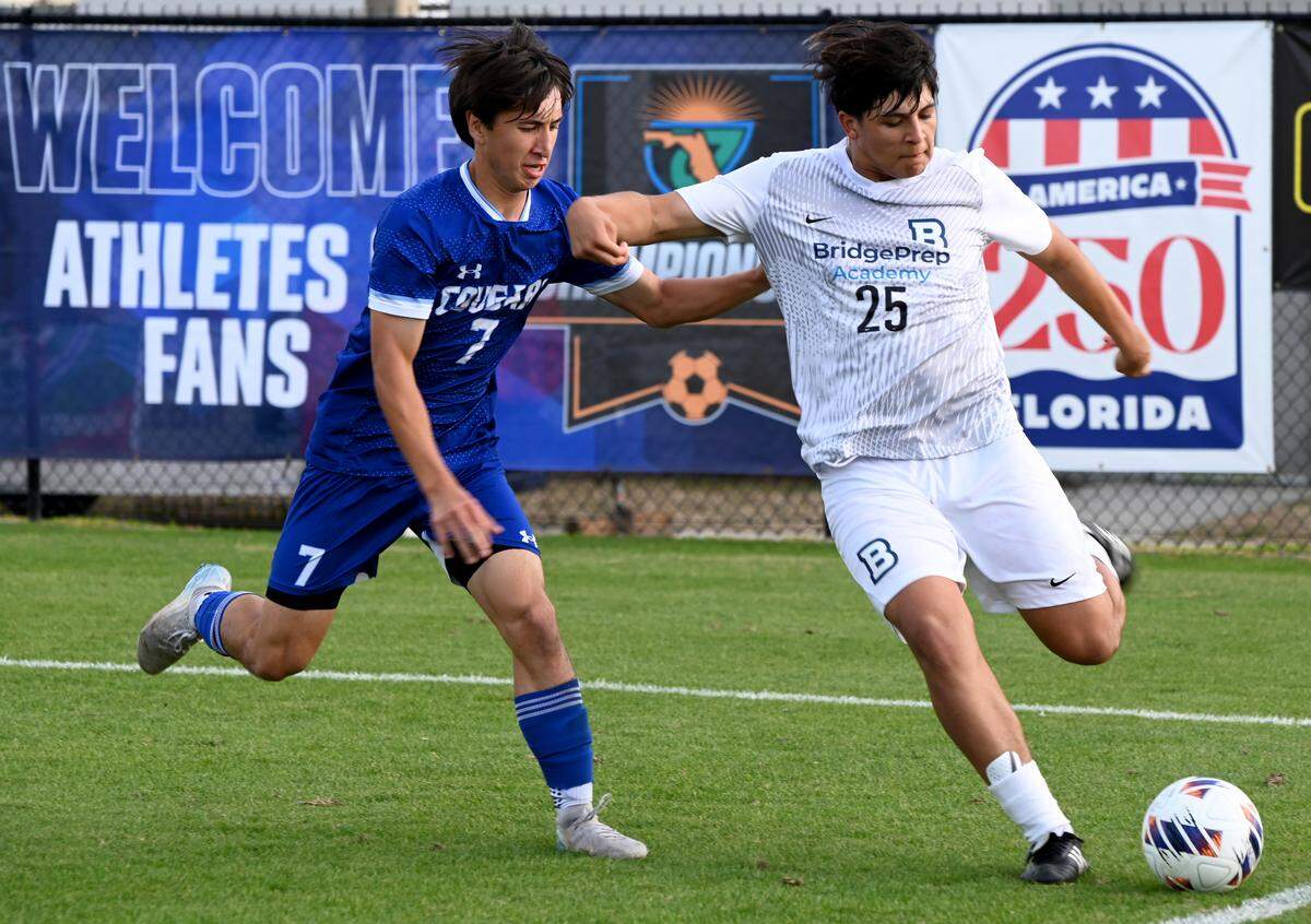 Bridgeprep junior Christopher Burgus unloads a shot down the sideline while Fort Myers Canterbury senior James Tomlinson moves into defend during a Class 1A boys soccer state semifinal on Friday at the Lake Myrtle Soccer Complex in Auburndale.