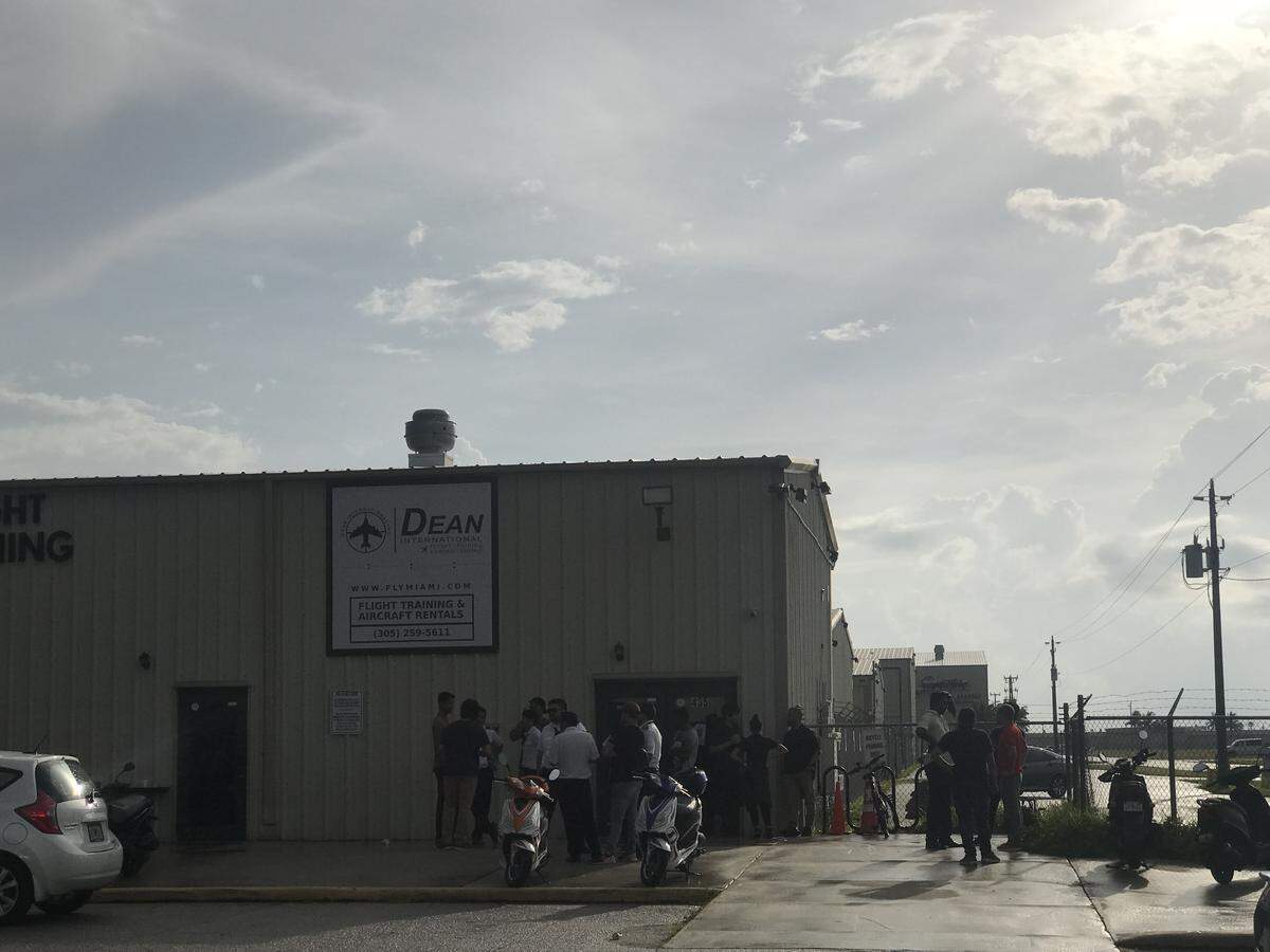 Students wait outside Dean International, the Miami-Dade flight school at Miami Executive Airport whose two planes collided in midair last week, killing four people. The owner of the school said Monday they will be closing, and the students are worried about getting their tuition refunded.