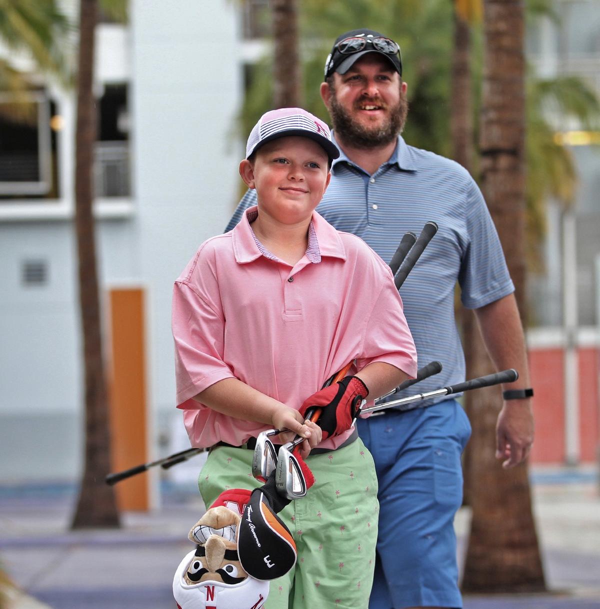 Kaiden Thompson, clubs in hand, and his father Dan Thompson of Naples head towards the Stadium Links venue to play a round of golf at Marlins Park on Sunday, January 20, 2019.