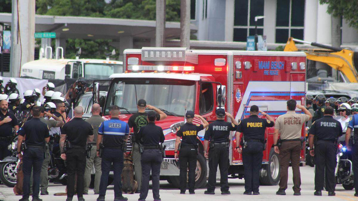 Police from different South Florida agencies salute as the body of Miami Beach police Officer David Cajuso is loaded into the back of an ambulance Tuesday, Oct. 28, 2025.