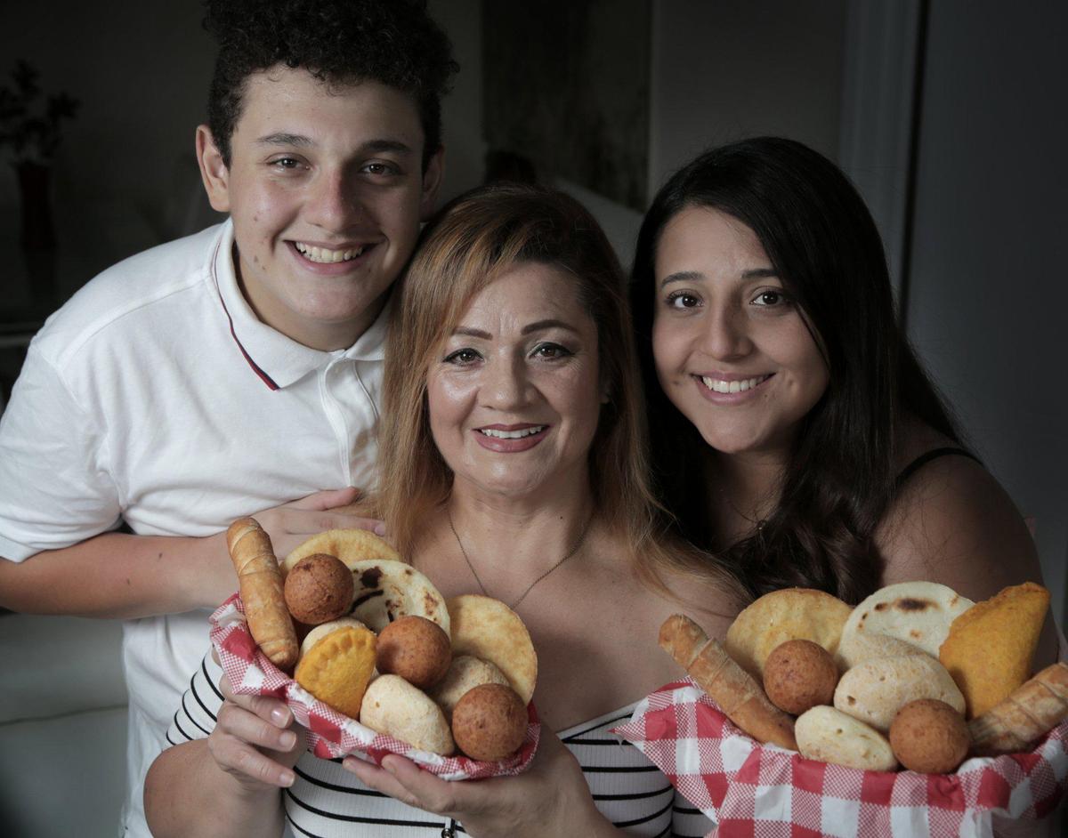 From left, Jorge Serrano, Carolina Galeano, and Nicole Serrano with baskets containing homemade tequeños, arepas de huevo, buñuelos, panes de bono, empanadas and arepas de queso in Miami, Florida, June 17, 2020.