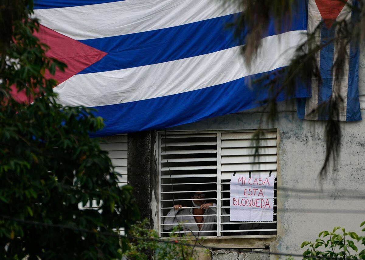 Yunior García Aguilera, playwright and one of the organizers of a protest march, stands next to a sign that reads in Spanish “My house Is blocked” that he posted on a window of his home, in Havana, Cuba, Sunday, Nov. 14, 2021. Cuban flags have been strung over the windows and doors of his home to stop him from communication to the outside.