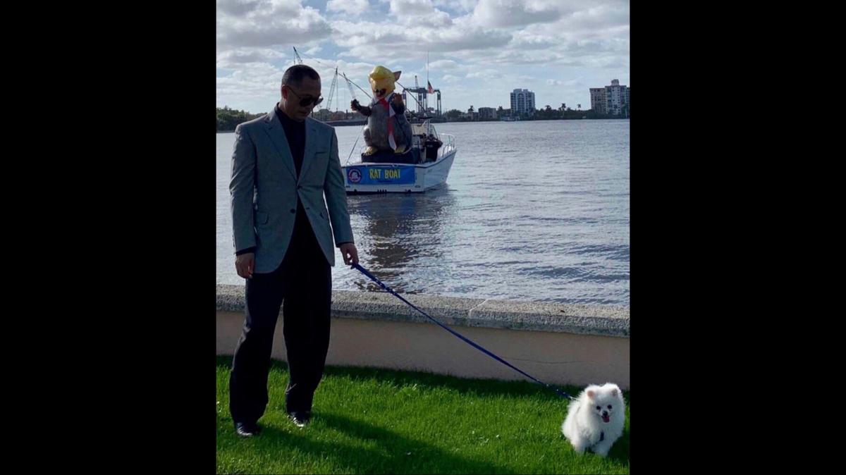A photo shows Guo Wengui walking his dog outside Mar-a-Lago in late December 2018 as anti-Trump protesters pulled up in a boat behind him.