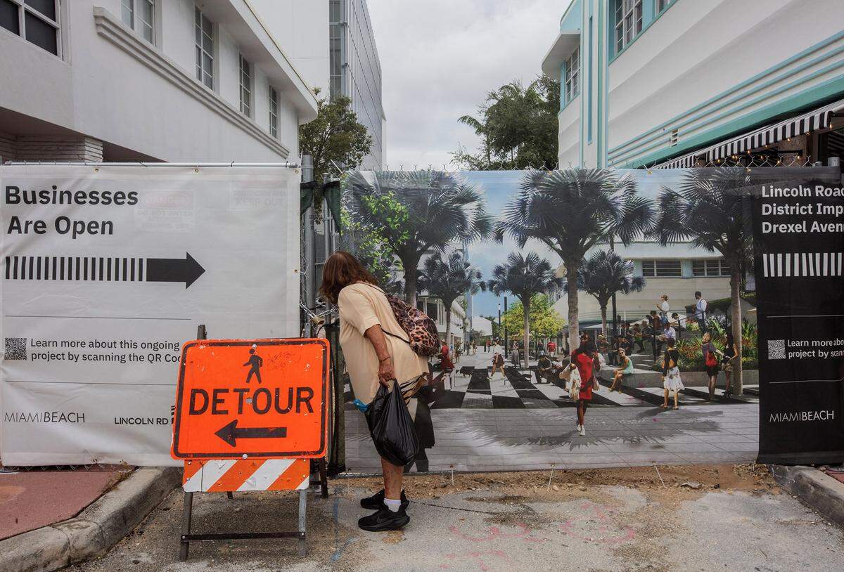 A woman peeks through a screened fence at construction at the intersection of Lincoln Road Mall and Drexel Avenue, where a long-delayed renovation of the famed pedestrian street broke ground in early September.