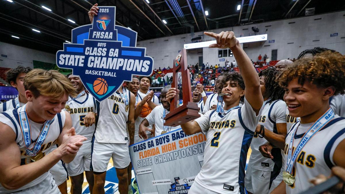 St. Thomas Aquinas Raiders DJ Sandi (2) holds the championship trophy as teammates celebrate the win over Evans for the FHSAA Class 6A Boys High School Basketball State Championship at the RP Funding Center in Lakeland, Florida on Saturday, March 8, 2025.