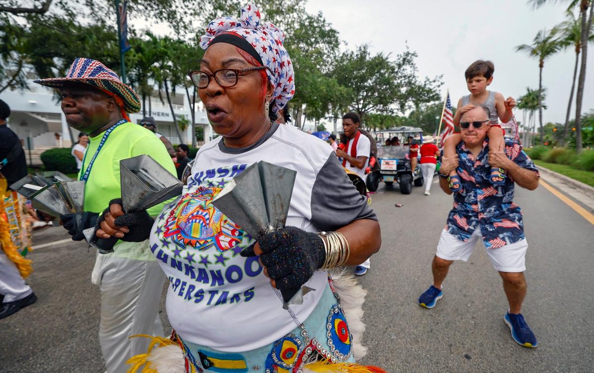 At right, Guy Loret-De-Mola, 70, carries Luca Jones, 4, as members of a Junkanoo band perform while residents, family and friends celebrate Independence Day during the 66th Annual Key Biscayne Fourth of July Parade on Key Biscayne, Florida on Friday, July 4, 2025.
