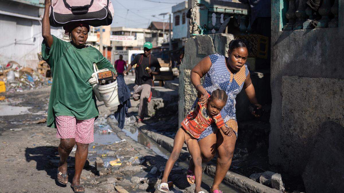 A woman carries a child during a fight between police and gang members in downtown Port-au-Prince, Haiti. More than 700,000 Haitians have been forced to leave their homes by the violence, half of them children.