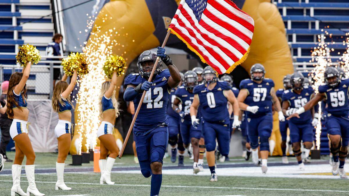 FIU Golden Panthers linebacker Reggie Peterson (42) carries the US flag as the team charges the field before the game against the Western Kentucky Hilltoppers at FIU Riccardo Silva Stadium in Miami on Saturday, November 25, 2023.