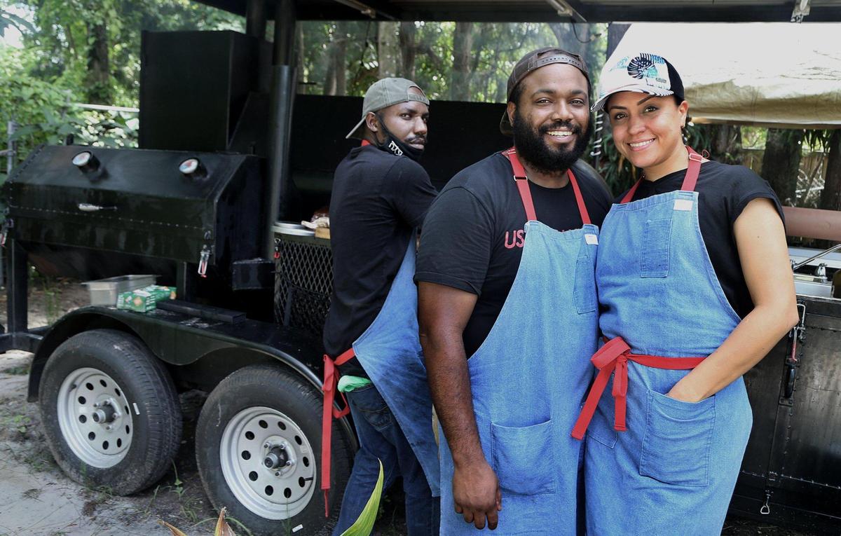 Chef Raheem Sealey (center) with his wife Yohanir Sandoval and his friend Chef Mark Wint, work at their recently opened pop up BBQ spot, The Drinking Pig.