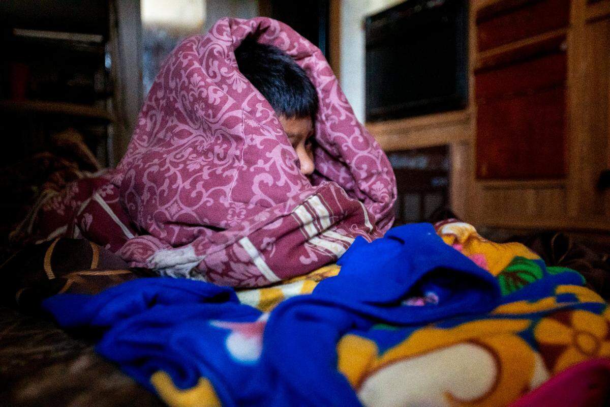 A migrant child wrapped in blankets is woken up by a Miami-Dade schools employee who has taken on the role of a distance learning teacher before a virtual class during the coronavirus pandemic in South Florida on Thursday, May 21, 2020.
