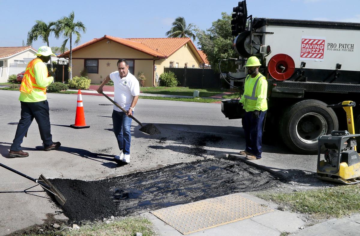 Commissioner Joe A. Martinez joins the work crew paving a pothole funded by Domino's Pizza in a marketing agreement with Miami-Dade to provide $5,000 to cover repairs in Martinez's suburban district.