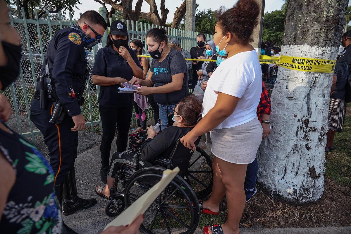 A police officer and a city staffer answer questions and direct residents as they navigate the long giveaway line. On Tuesday, December 15, 2020, a long line formed around the Juan Pablo Duarte Park as Miami residents stood in line for hours while the City of Miami gave away about 500 grocery gift cards under the coordination of volunteers, city staff, and Miami Police officers.