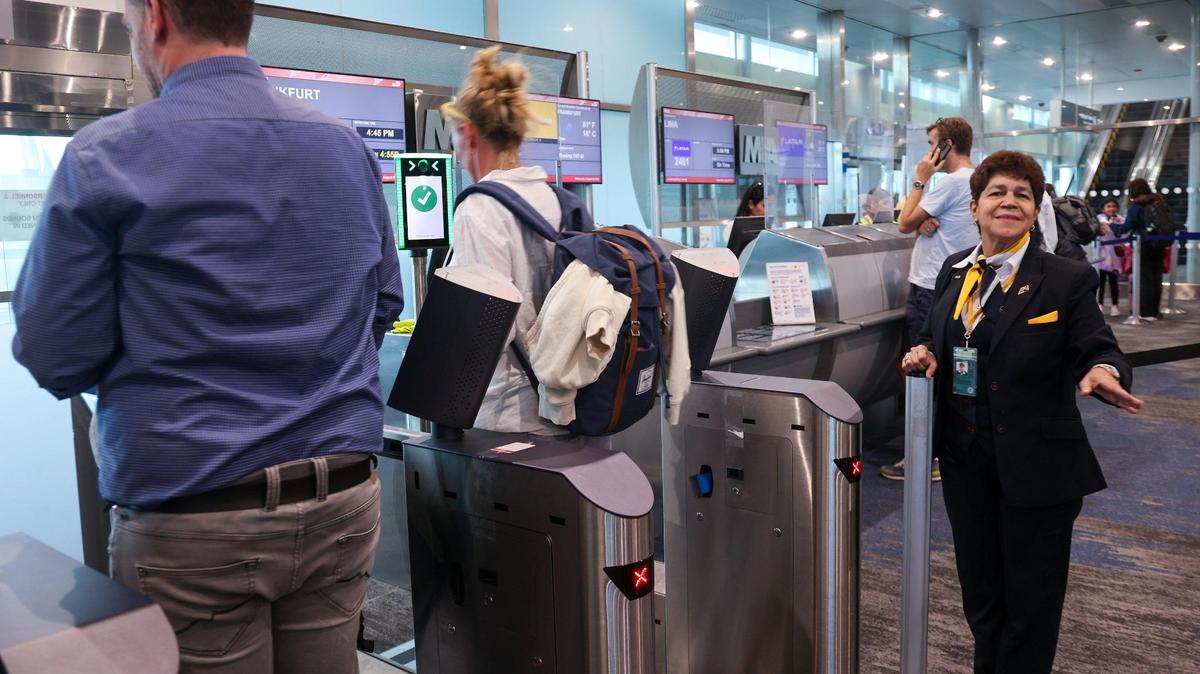 Eva Burgos, agente de servicio al pasajero (derecha) en el Aeropuerto Internacional de Miami ayuda a los pasajeros a embarcar en el vuelo 463 de Lufthansa a Francfort, el 9 de agosto de 2023, usando la nueva tecnología de reconocimiento facial en la puerta J17 del aeropuerto de Miami.