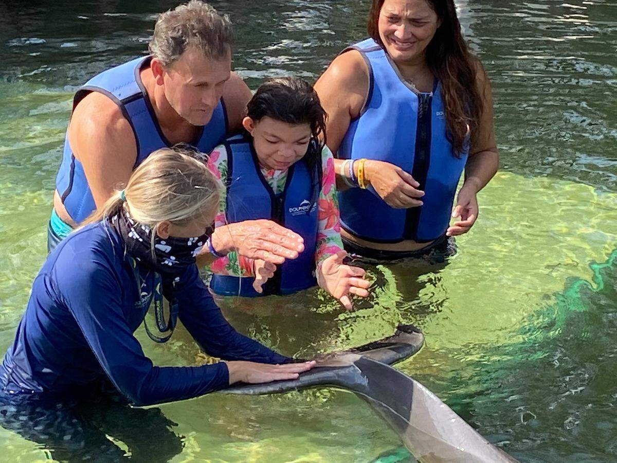 Marine mammal trainer Anna Whisenhunt shows Giovanna Camarotti Dadalto how to pet the fluke of Leo the dolphin at Dolphins Plus in Key Largo. Her parents, Renan Dadalto and Mirella Pucci look on. The family went to Dolphins Plus Friday, April 23, 2021, as part of the Make-A-Wish South Florida program.