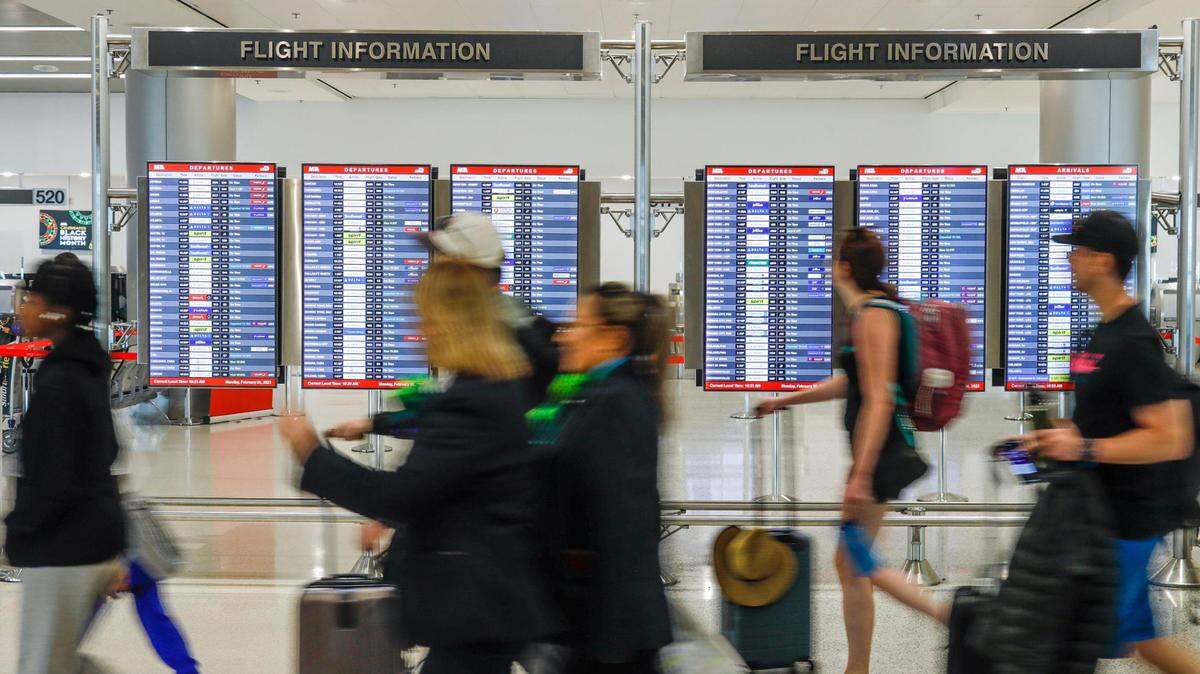 Passengers walk by flight information screens at Miami International Airport on Monday, Feb. 6, 2023.