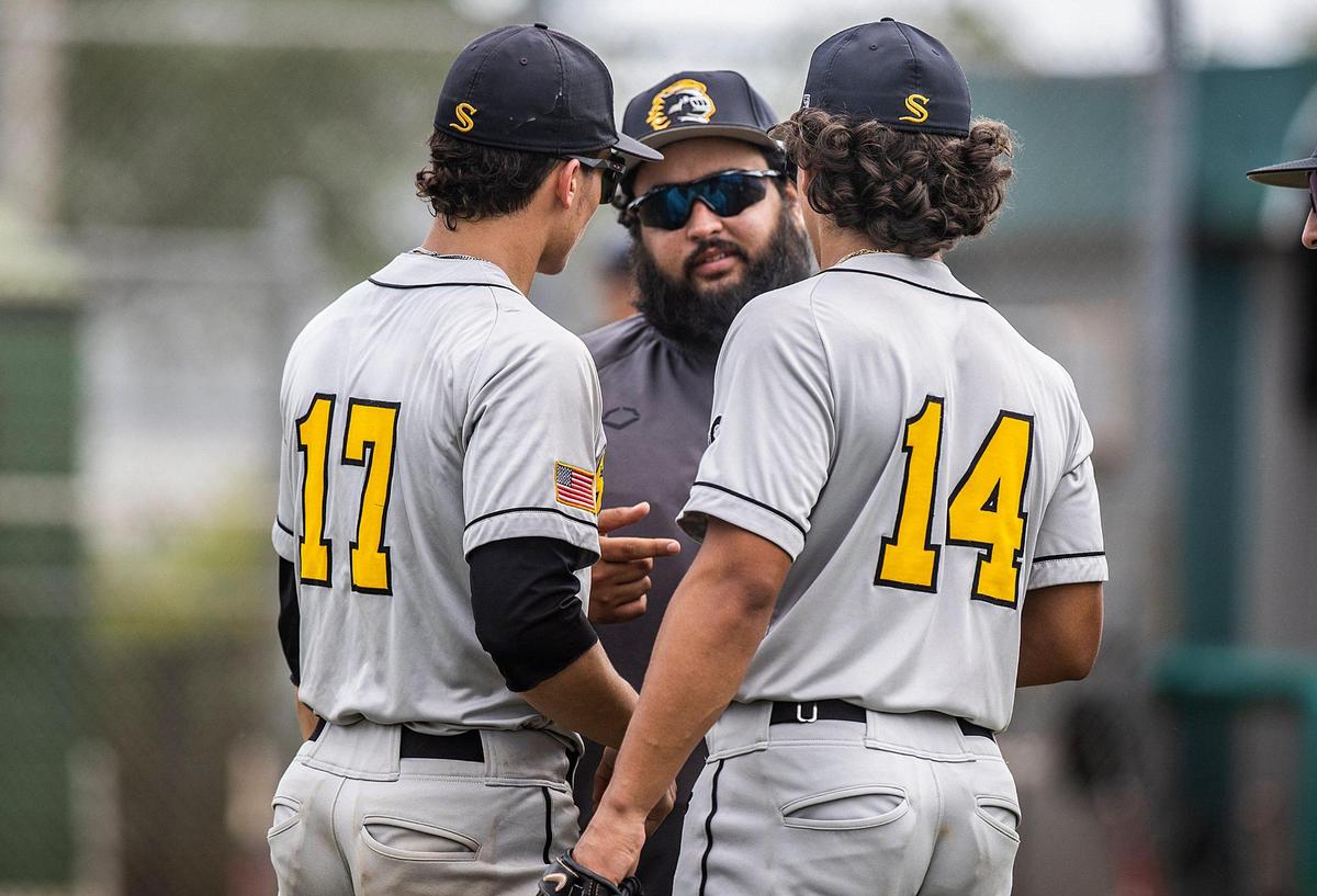 Miami Sunset Knights’s head coach Julio Mendoza talks to players Andres Gonzalez #17 (RHP/OF) and Daniel Reyes #14 (OF), runs after hitting a hit in the first inning of a GMAC Tournament game against theFelix Varela Vipers at the Felix Varela Senior High School baseball field in Kendall, on Friday April 14, 2023