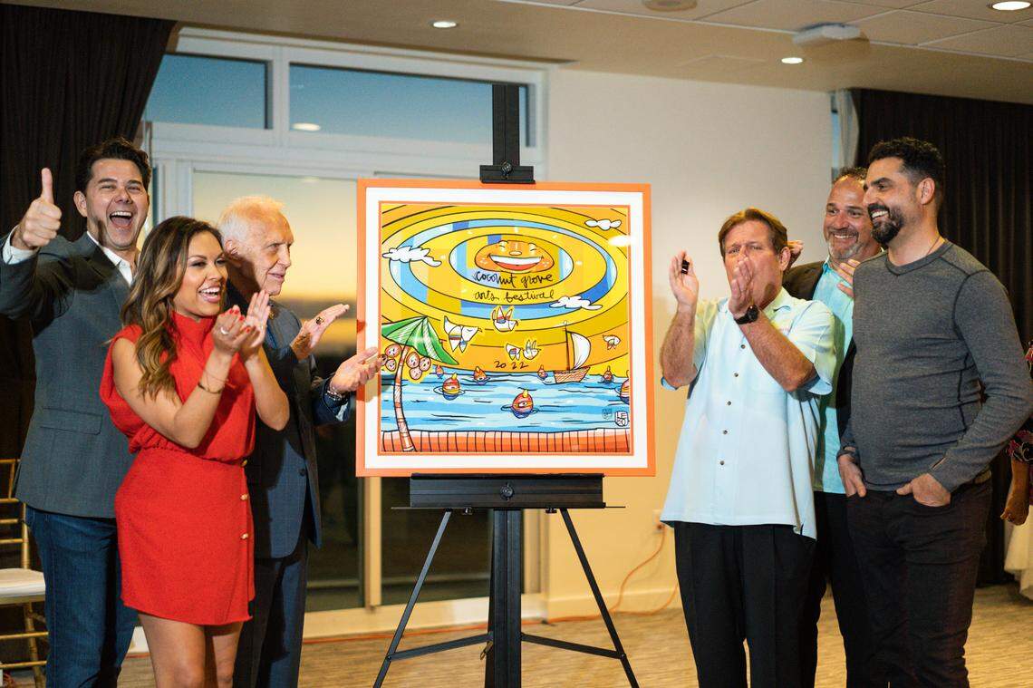 Artist David Le Batard, known as Lebo, stands at right as his poster for the 2022 Coconut Grove Arts Festival is unveiled Feb. 4. Festival president Monty Trainer stands left of the poster.