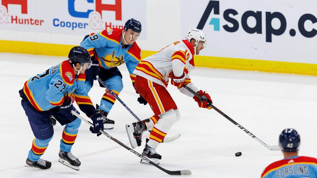 Calgary Flames center Jonathan Huberdeau (10) drives down the ice with the puck against Florida Panthers left wing Matthew Tkachuk (19) and Panthers center Eetu Luostarinen (27) during the third period of an NHL game at FLA Live Arena on Saturday, November 19, 2022 in Sunrise, Fl.