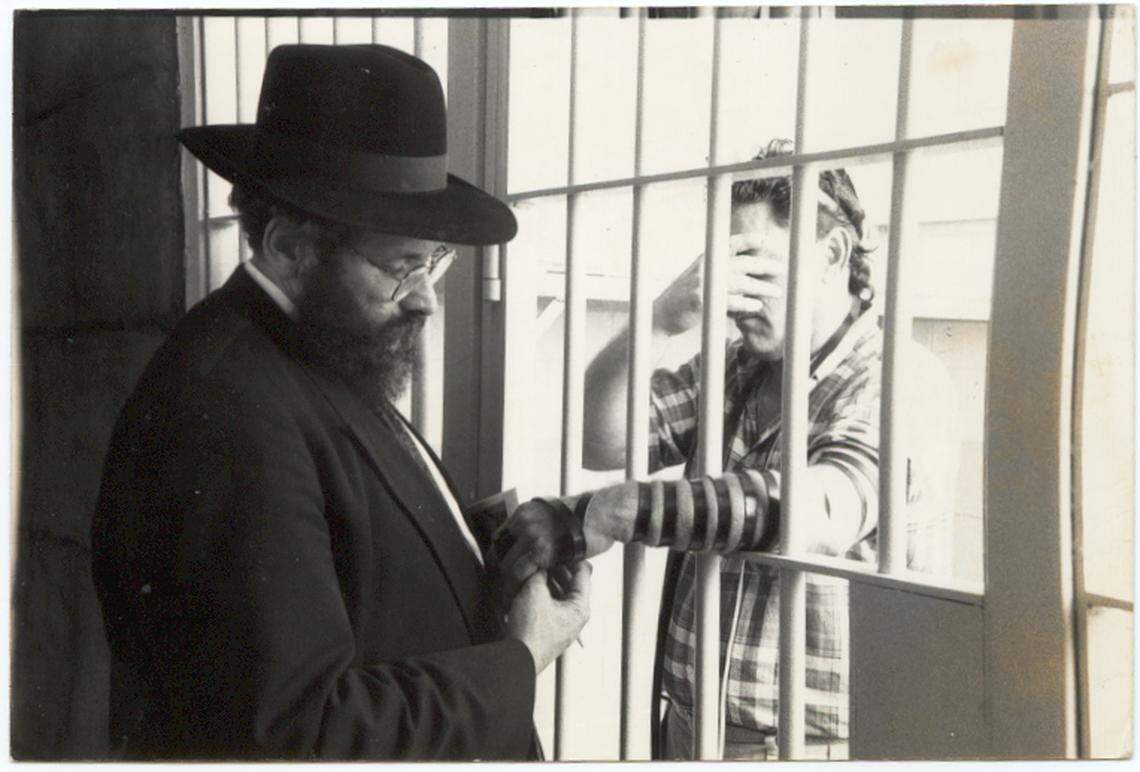 Rabbi Sholom Lipskar puts on Tefillin through prison bars. Lipskar, who founded the Shul of Bal Harbour and the Aleph Insitute, was known as a compassionate spiritual leader in the Orthodox community