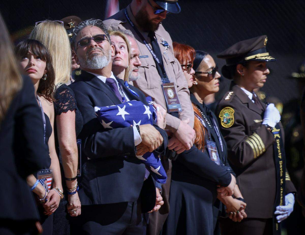 Isabella, sister, left, David, father, and Yolanda Jaramillo, mother, center, look skyward during a flyover in the final honors of the funeral service for Miami-Dade Sheriff’s Deputy Devin Jaramillo at loanDepot Park, Tuesday, Nov. 18, 2025, in Miami, Florida. 