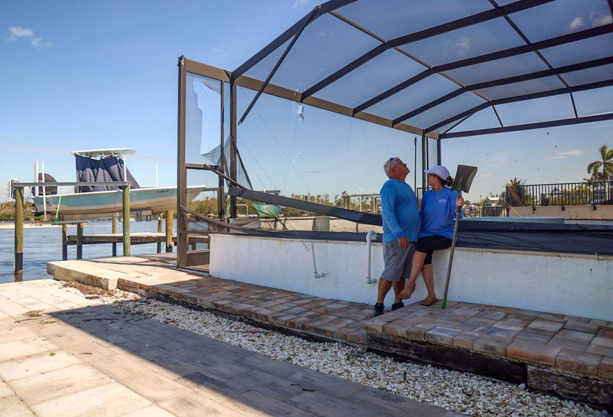 Home builder Steve Ondrejka, 58, left, and wife, Andrea, 57, take in the damage to the pool screen at their Matlacha home as they take a short break from cleaning mud from Hurricane Milton.
