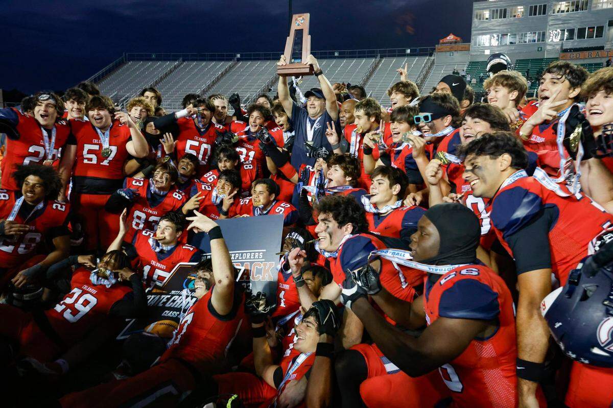 Columbus Explorers head coach Dave Dunn holds the championship trophy as the team celebrates defeating the Mandarin Mustangs in the FHSAA State Championships, Class 4M, at Bragg Memorial Stadium in Tallahassee, Florida, on Friday, December 8, 2023.