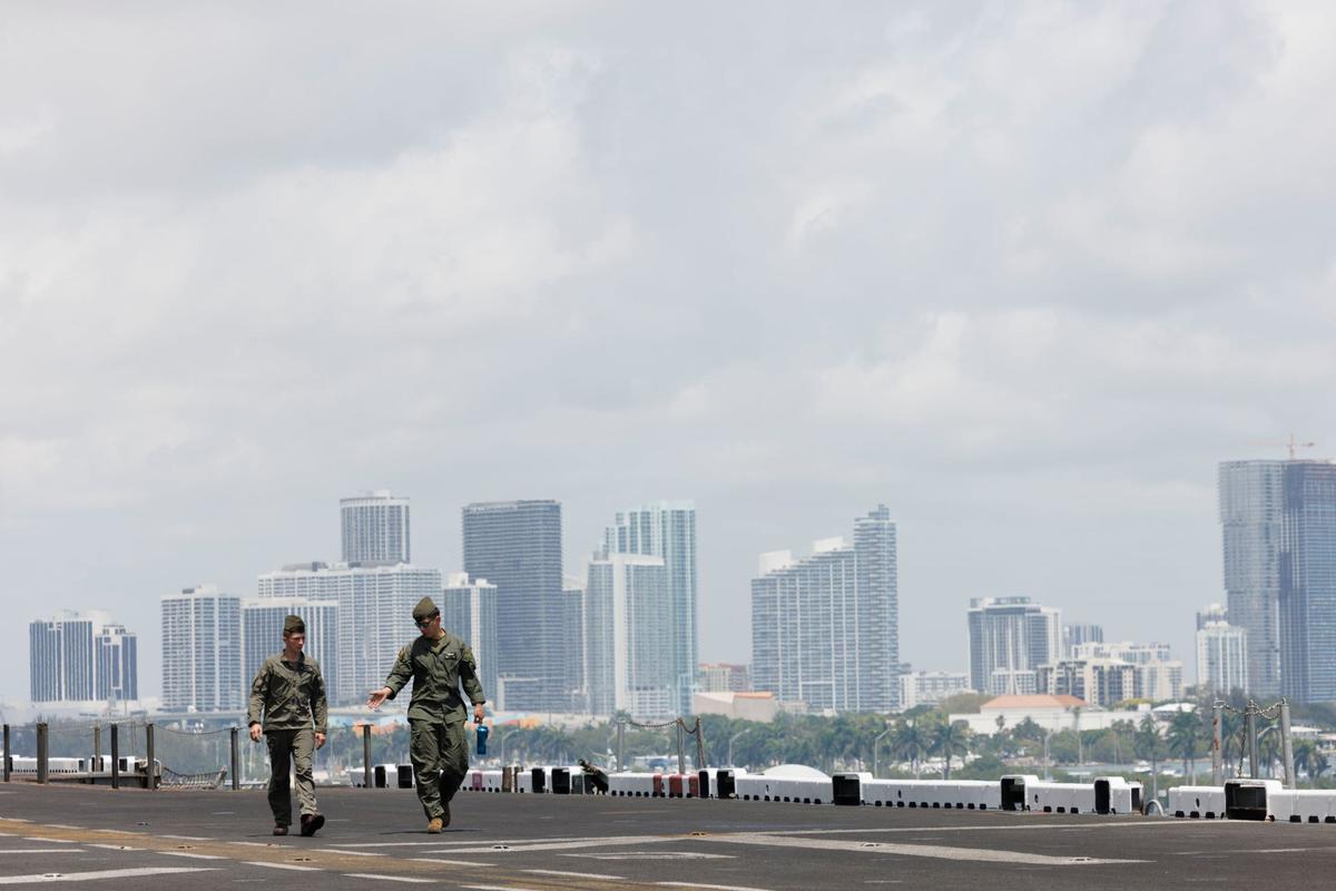 Two members of a heavy marine helicopter squadron walk across the flight deck of the USS Bataan in front of the Miami skyline during the opening day of Fleet Week on Monday, May 6, 2024, at Norwegian Cruise Lines Terminal in PortMiami.