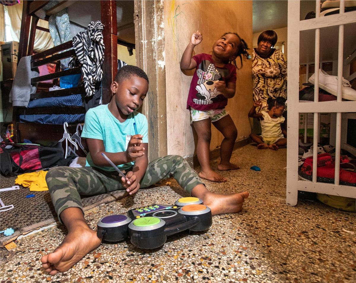 Joan Pratt watches over her grandchildren as Loyal plays drums in the hallway of their Liberty City home and Abigail dances. Far right with Pratt is Terylin.