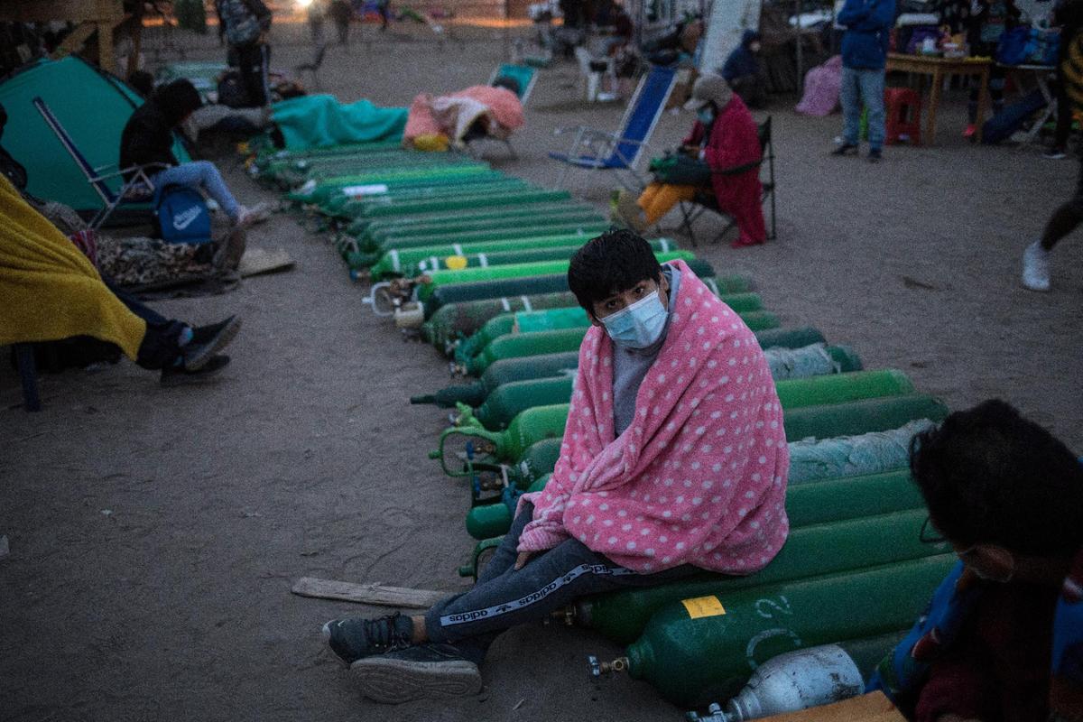 A man sits on top of empty oxygen cylinders, waiting for a shop to open to refill his tank, in the Villa El Salvador neighborhood, as the lack of medical oxygen to treat COVID-19 patients continues in Lima, Peru, Tuesday, April 6, 2021.