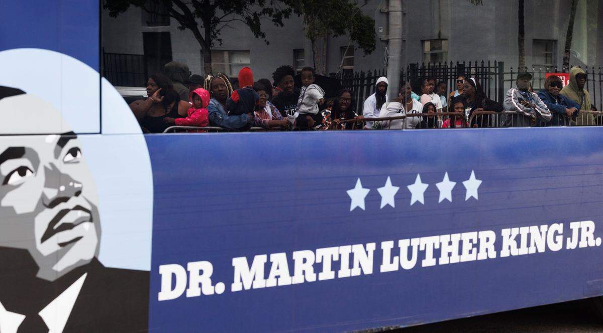 The reflection of parade attendees is seen through a buss driving in the Dr. Martin Luther King Jr. Day parade on Monday, Jan. 20, 2025, in Liberty City in Miami, Fla.