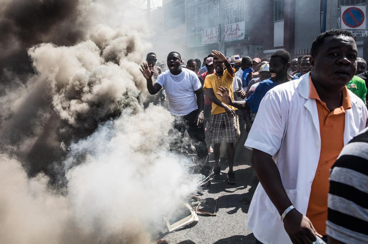 Protesters, medical professionals, and political opponents walk past burning trash during a demonstration demanding the resignation of President Jovenel Moise in the Haitian capital in Port-au-Prince on Oct. 30, 2019.