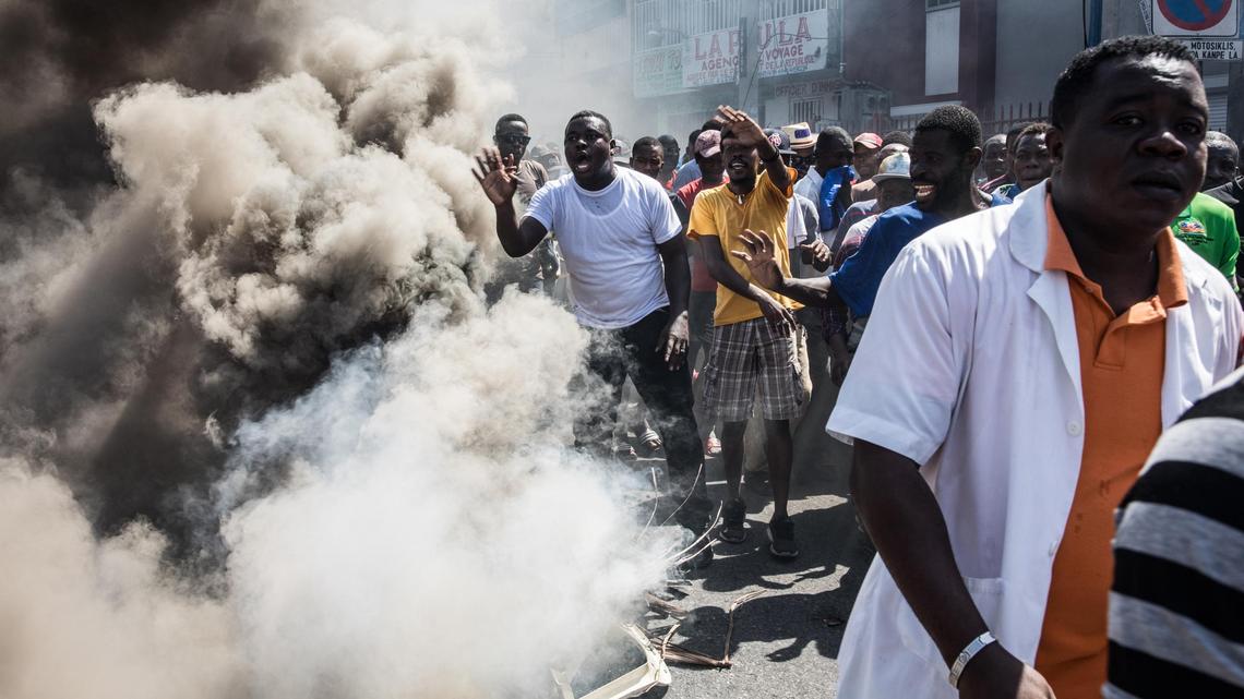 Protesters, medical professionals, and political opponents walk past burning trash during a demonstration demanding the resignation of President Jovenel Moise in the Haitian capital in Port-au-Prince on Oct. 30, 2019. In the midst of the crisis, an attempted jail break resulted in the rape of 10 women detainees, human-rights groups say.