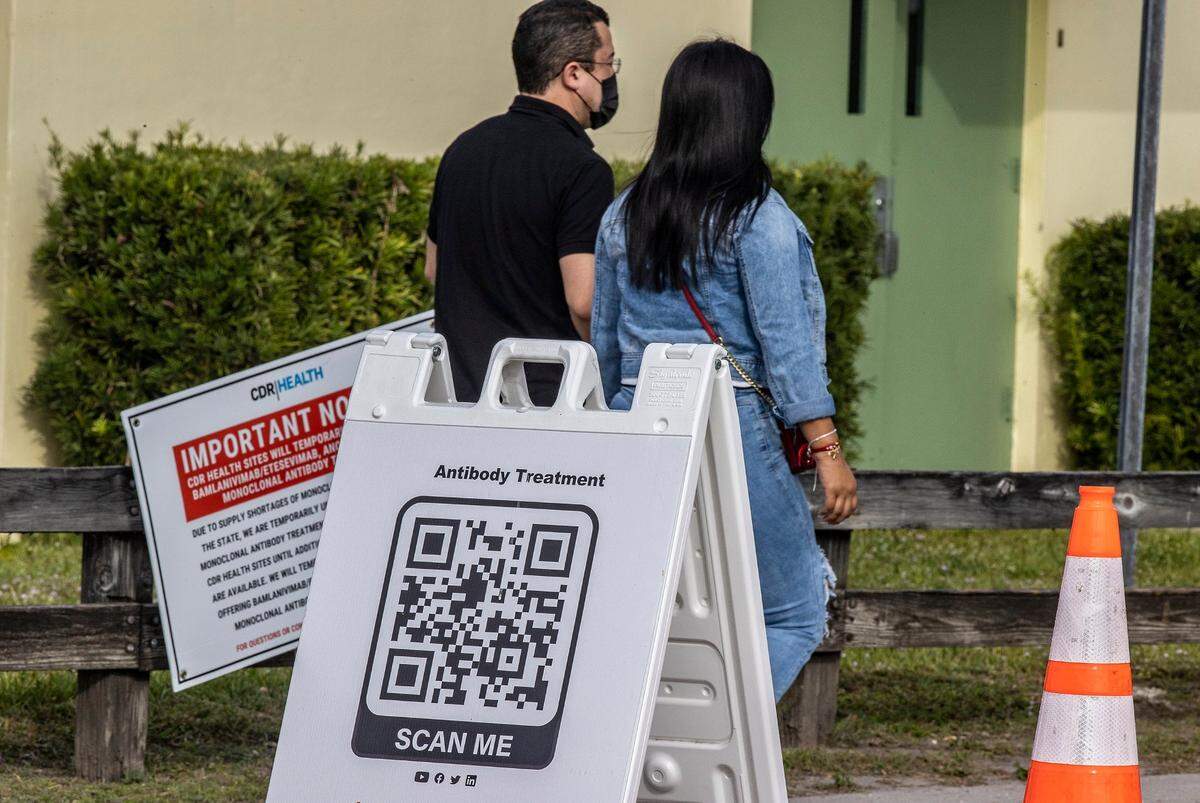 A couple walk by a QR code outside of a monoclonal antibodies distribution site to treat COVID-19, at Tropical Park on Tuesday afternoon, Jan. 4, 2021.