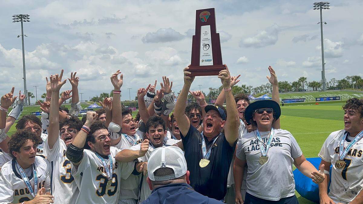 St. Thomas Aquinas boys’ lacrosse coach Terry Crowley holds up the state championship trophy as the Raiders celebrate their fourth state championship on Saturday afternoon in Naples, Fla.