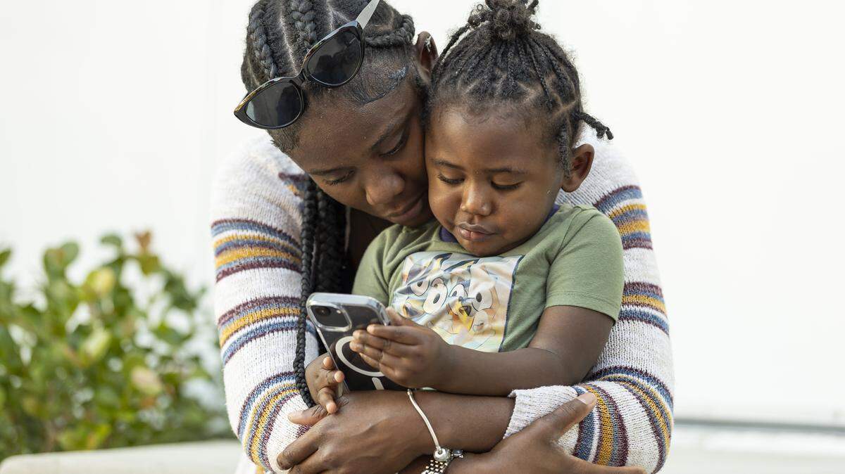 Nathalia Hall, 18, hugs her son, Rhylan Hall, 2, as he plays on her phone near the Lotus House Women’s Shelter. Hall is struggling to find stable housing.