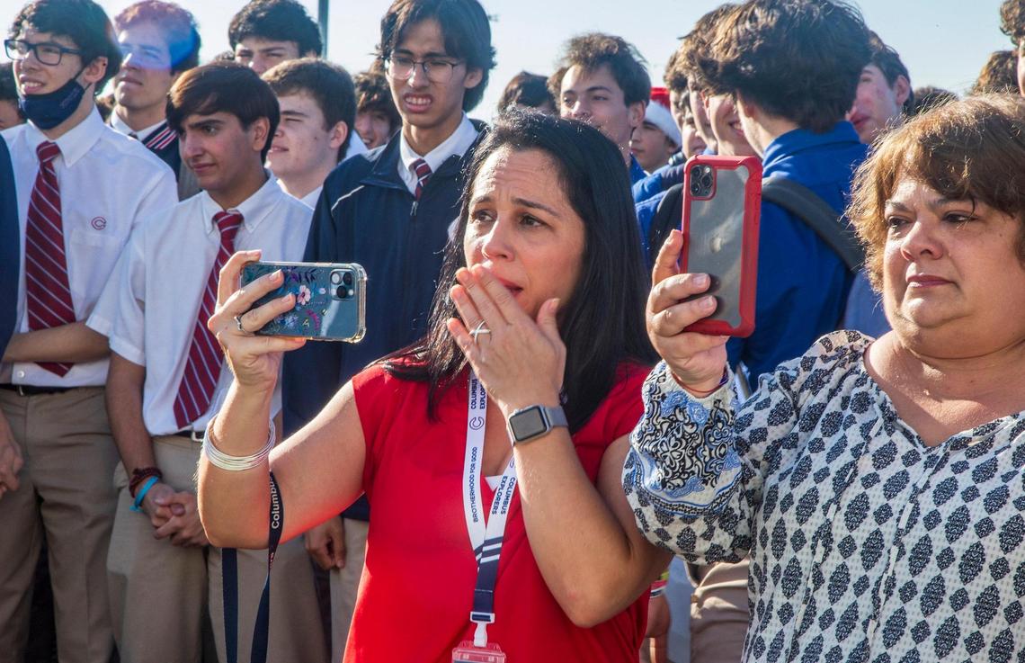 Christopher Columbus High School staff member Marisa Da Silva, left, reacts after entrepreneur and TV personality Marcus Lemonis surprised everyone announcing his donation of $10 million to build two centers and to cover $18,000 checks for all staff and employees at his alma mater in Miami, on Thursday, Dec. 9, 2021.