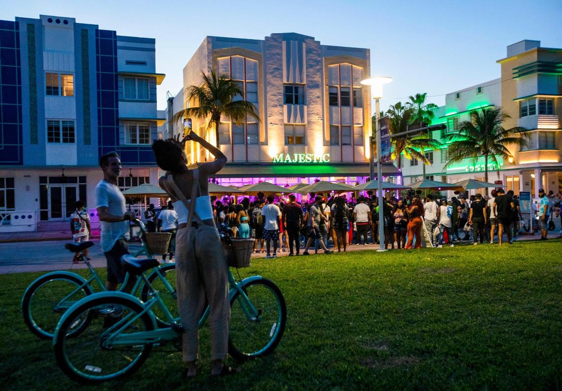 A woman stops during a bike ride to take a photo of crowds before curfew on Ocean Drive in Miami Beach, Florida, on Sunday, March 28, 2021.